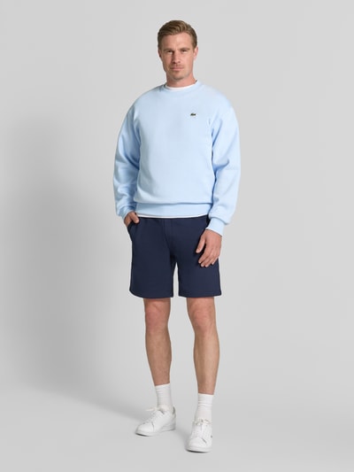 Męski model nosi Regular Fit Sweatshirt aus Baumwoll-Mix od Lacoste, jasnoniebieska bluza, gładka faktura, Ganzkörperansicht von vorne.