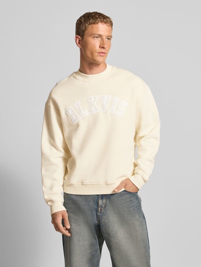 Männermodel trägt Sweatshirt mit Logo und Rundhalsausschnitt von BLKVIS in Creme, Relaxed-Fit, reine Baumwolle, Ganzkörperansicht von vorne.