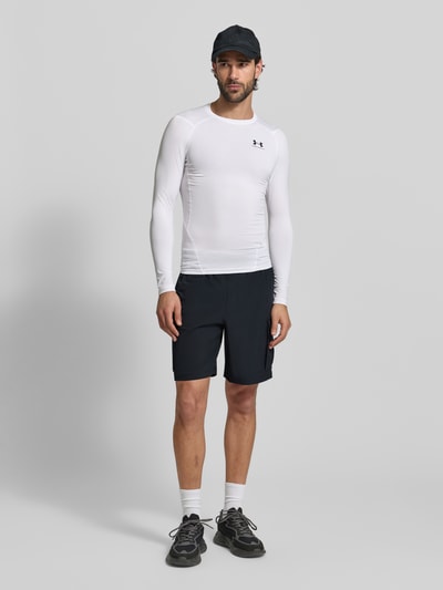 Männermodel trägt Straight Fit Shorts mit Cargo-Taschen Modell 'Vibe' von Under Armour in Schwarz, elastischer Bund, Logo-Print, Ganzkörperansicht von vorne.