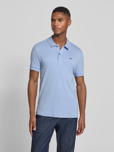 Männermodel trägt Regular Fit Poloshirt aus reiner Baumwolle von Lacoste in Hellblau, unifarben, Logo-Detail, Ganzkörperansicht von vorne.