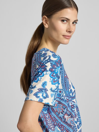 Kobiece model prezentuje damski t-shirt T-Shirt mit Allover-Look od Oui, mieszanka materiałów z dodatkiem streczu, krój regular fit, wzór na całej powierzchni, okrągły dekolt, długość tyłu w rozmiarze 36: 50 cm, długość rękawów w rozmiarze 36: 19 cm, kolor niebieski z bielą, prosty fason, lekko błyszcząca tekstura. Zbliżenie na górną część ciała.