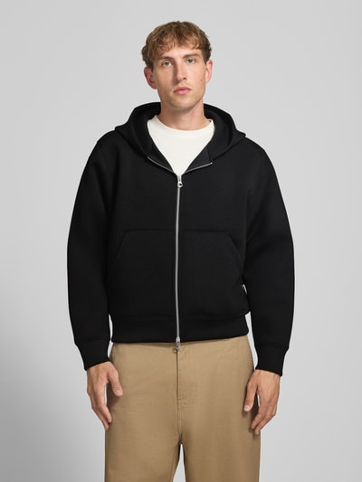 Männermodel trägt schwarze Relaxed Fit Sweatjacke mit Zweiwege-Reißverschluss von JACK & JONES, Känguru-Tasche, Nahaufnahme Oberkörper.
