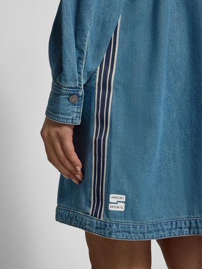 Frauenmodel trägt knielanges Jeanskleid mit Stehkragen von Marc Cain, blauer Baumwoll-Lyocell-Mix, Used-Look, Detailaufnahme Saum und Ärmel.