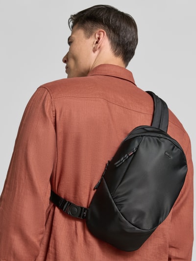 Männermodel trägt Umhängetasche mit Label-Applikation Modell 'AYDEN_NEW_NS' von HUGO, unifarbene Optik, Reißverschluss, Hauptfach, Reißverschlussfach, Einschubfach, Schulterriemen, Ganzkörperansicht Rückansicht