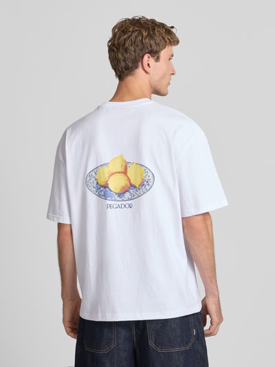 Männermodel trägt Oversized T-Shirt mit Backprint von PEGADOR, reine Baumwolle, weiß, lockere Passform, Teller-Motiv, Ganzkörperansicht Rückansicht.