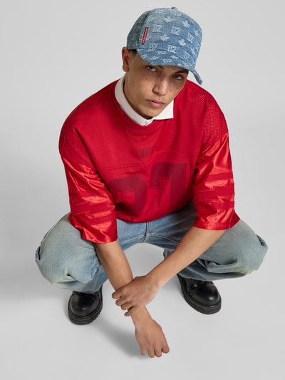 Männermodel trägt Base Cap in Denim-Optik von Dsquared2 mit Allover-Logo-Details aus reiner Baumwolle, Ganzkörperansicht von vorne.
