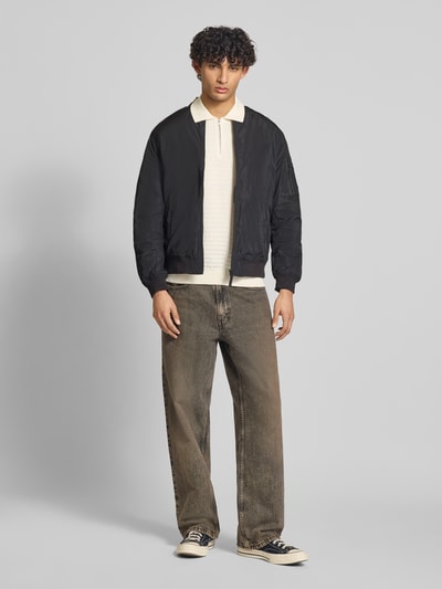 Männermodel trägt Regular Fit Poloshirt aus reiner Baumwolle Modell 'MENU' von Only & Sons mit Flechtoptik und kurzem Reißverschluss, Ganzkörperansicht von vorne.