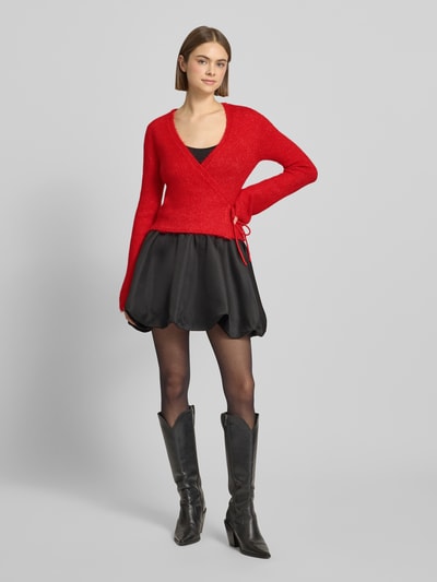 Frauenmodel trägt Cardigan in Wickel-Optik von Gina Tricot in Rot, Material-Mix mit Alpaka-Anteil, Slim-Fit, V-Ausschnitt, Ganzkörperansicht von vorne.