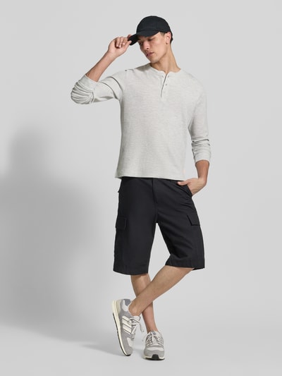 Männermodel trägt Regular Fit Longsleeve in Strick-Optik Modell 'Niagara' von Jack & Jones, hellgrau, Henley-Ausschnitt, Nahaufnahme Ganzkörperansicht von vorne. Baumwoll-Mix, Rückenlänge 65 cm bei Größe M, kombiniert mit dunklen Shorts und Sneakern.