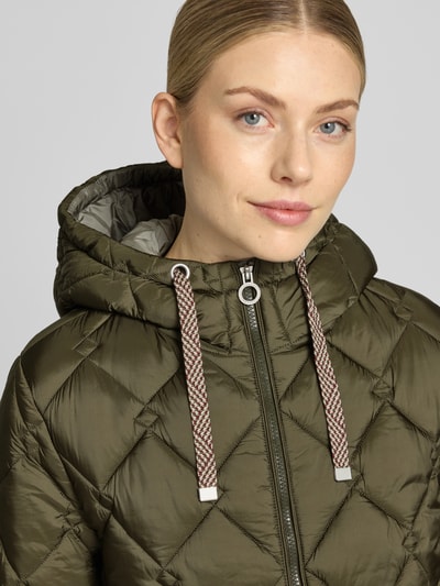 Kobieta nosi Regular Fit Mantel in Stepp-Optik od FUCHS SCHMITT, z kapturem i kieszeniami, oliwkowy, tekstura pikowana, zbliżenie górnej części ciała. Szerokość w rozmiarze 36: 41 cm, długość tyłu: 70 cm, szerokość klatki piersiowej: 53 cm, długość rękawa: 64 cm.