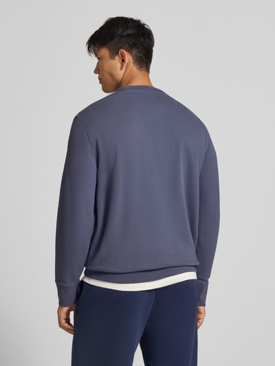 Männermodel trägt Sweatshirt aus Baumwoll-Mix von Superdry in Blau, lockere Passform, Rückansicht, Kontext: Herren Sweatshirt, Rundhalsausschnitt, elastische Abschlüsse, Label-Stitching, Rückenlänge 66 cm, Ärmellänge 62 cm. Ganzkörperansicht Rückansicht