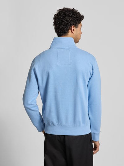 Mannenmodel draagt Regular Fit sweatshirt met logo-stitching van Superdry in lichtblauw, katoenmix, opstaande kraag met ritssluiting, elastische boorden, ruglengte maat M 65 cm, mouwlengte maat M 63 cm. Ganzekörperaanzicht achteraan.