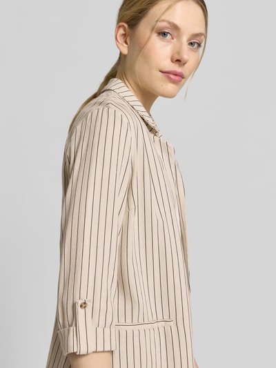 Frauenmodel trägt Loose Fit Kurzblazer aus Viskose-Leinen-Mix Modell 'JESMILO' von Vero Moda, beige mit feinen schwarzen Streifen, Flammgarnstruktur, 3/4-Arm mit fixiertem Umschlag, angedeutete Paspeltaschen, Reverskragen, unifarbene Optik, Nahaufnahme Oberkörper.