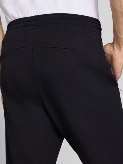 Männermodel trägt schwarze Sweatpants mit Label-Detail von Champion, Baumwoll-Mix, elastischer Bund, Detailaufnahme Rückenansicht.
