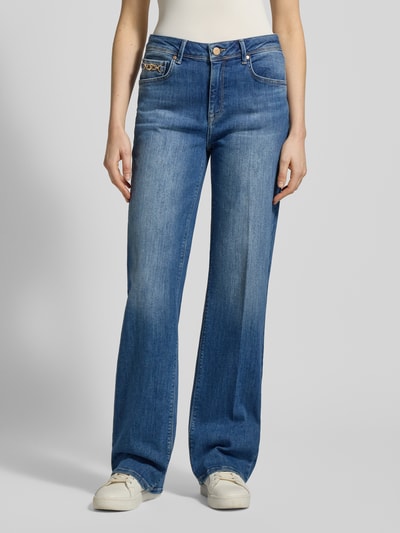 Frauenmodel trägt Straight Fit Jeans aus Baumwoll-Mix Modell 'KIRA' von Raffaello Rossi in mittelblau mit Kontrastnähten, 5-Pocket-Design, Zier-Applikation in Gliederketten-Optik, Ganzkörperansicht von vorne.