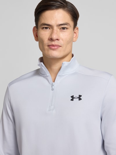 Männermodel trägt Sweatshirt mit Label-Detail von Under Armour in Hellgrau mit Stehkragen, kurzem Reißverschluss, gerippte Abschlüsse, Nahaufnahme Oberkörper. Rückenlänge 72 cm, Ärmellänge 67 cm, lockerer Schnitt, Größe M.