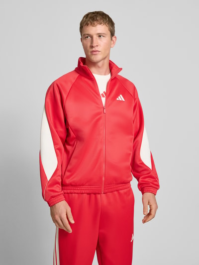 Männermodel trägt Trainingsjacke mit Stehkragen und Logo von adidas Sportswear in Rot mit weißen Details, Regular Fit, Nahaufnahme Oberkörper.