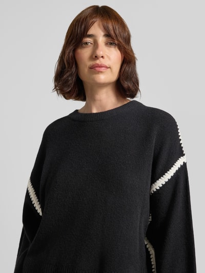 Frauenmodel trägt Strickpullover mit Rundhalsausschnitt und Kontraststreifen von Oui, Schwarz mit weißen Akzenten, Material-Mix, Relaxed Fit, Nahaufnahme Oberkörper.