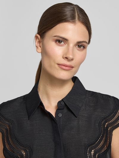 Modelka kobieca nosi Regular Fit Blusentop aus Modal-Mix Modell 'COLE' od Copenhagen Muse, mieszanka modalu, kołnierzyk koszulowy, zakryta listwa guzikowa, damska bluzka, długość tyłu w rozmiarze S: 59 cm, czarny kolor, faktura lekko półtransparentna, delikatne faliste wstawki na ramionach, zbliżenie górnej części ciała.