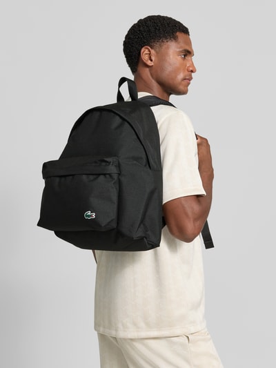 Mężczyzna nosi plecak z przegródką na laptop Rucksack mit Laptopfach od Lacoste, czarny, tekstura materiałowa, Ganzkörperansicht von der Seite, Herren kosmetyczka od Lacoste.