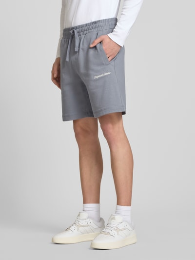 Männermodel trägt Shorts mit Label-Stitching Modell 'KARL' von Jack & Jones, Baumwoll-Mix, Relaxed-Fit, seitliche Eingrifftaschen, Ganzkörperansicht von vorne.