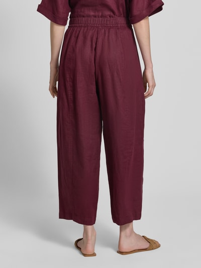 Frauenmodel trägt Leinenhose in verkürzter Passform mit elastischem Bund von Christian Berg Woman, weinrot, Wide Leg, reine Leinen, Ganzkörperansicht Rückansicht.