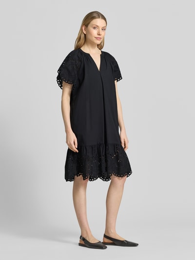 Modelka kobieca ma na sobie Relaxed Fit Minikleid mit floraler Lochstickerei od Christian Berg Woman Selection, czarna czysta bawełna, florystyczna ażurowa tkanina, tunikowy dekolt, krótkie rękawy, Szerokość w rozmiarze 36: 34 cm, długość tyłu 74 cm, długość rękawa 26 cm, widok całej sylwetki z przodu.