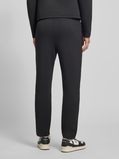 Männermodel trägt Tapered Sweatpants mit Baumwoll-Anteil von Lacoste, efekt: jednolity kolor, krój tapered, naszywka z logo, tunel, ściągacz, boczna kieszeń zapinana na zamek błyskawiczny, wykończenie materiału: scuba, Ganzkörperansicht Rückansicht