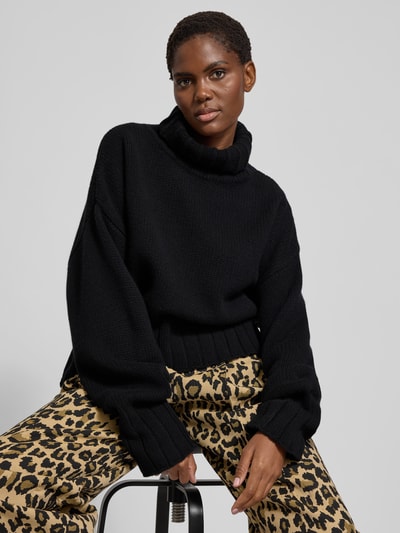 Frauenmodel trägt Oversized Pullover mit Rollkragen von black palms aus reiner Wolle mit gerippten Abschlüssen, Farbe Schwarz, Nahaufnahme Oberkörper.