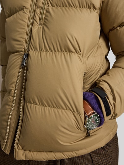 Männermodel trägt Regular Fit Daunenjacke mit Logo-Stitching von Polo Ralph Lauren in Beige, sichtbare Steppnähte, Nahaufnahme Oberkörper. Herren Daunenjacke von Polo Ralph Lauren.