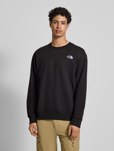 Męski model nosi Bluza z nadrukiem z logo od The North Face z bawełny, krój relaxed fit, prążkowane wykończenia, okrągły dekolt, długość tyłu 70 cm, długość rękawów 65 cm, kolor czarny, gładka faktura, nadruk z logo, całkowity widok z przodu.