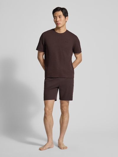 Männermodel trägt Regular Fit Pyjama-Oberteil aus Baumwoll-Mix Modell 'WAFFLE' von BOSS in Braun, Struktur Piqué, Kurzarm, Label Stitching, Ganzkörperansicht von vorne.
