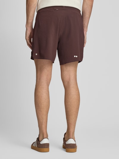 Męski model nosi szorty z elastycznym paskiem z logo model 'SENSE AERO' od Salomon, mieszanka materiałów z dodatkiem streczu, krój loose fit, nadruk z logo, kolor brązowy, szerokość w rozmiarze M: 38 cm, długość wewnętrzna nogawki: 18 cm, widok całej sylwetki z tyłu.