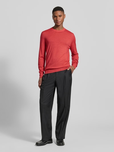 Männermodel trägt Strickpullover aus reiner Schurwolle von GRAN SASSO in Rot, körpernaher Schnitt, schwarze Hose, Ganzkörperansicht von vorne.