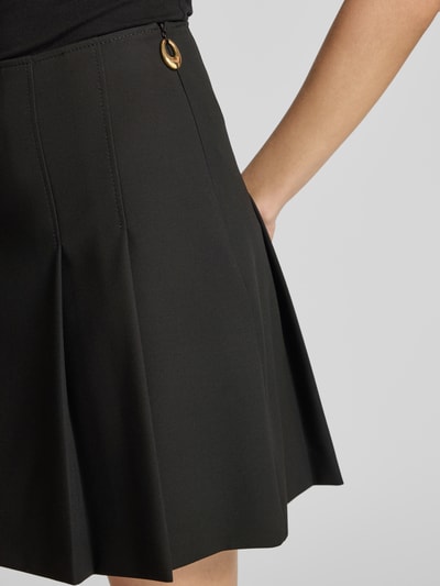 Vrouwenmodel draagt A-lijn plissérok met label-zipper, unikleur, mini-lengte, HUGO Roballo, detailopname heupzijde.