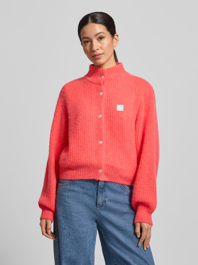 Frauenmodel trägt Strickjacke mit Knopfleiste von American Vintage in Pink, lockerer Schnitt, Stehkragen, gerippte Abschlüsse, Nahaufnahme Oberkörper.