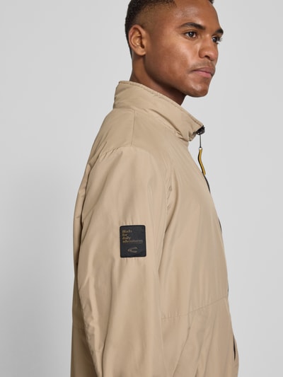 Männermodel trägt Blouson mit Logo-Print und Stehkragen von camel active in Beige mit Label-Patch, Nahaufnahme Oberkörper seitlich.