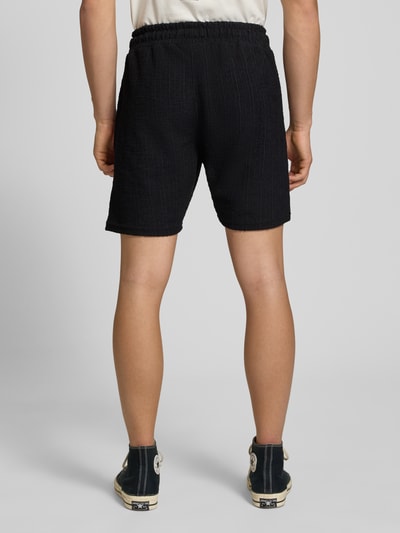 Männermodel trägt Shorts mit Label-Patch Modell 'LIBCO' von Pegador, Schwarz, Strukturmuster, Material-Mix, Gerader-Schnitt, elastischer Bund, Ganzkörperansicht Rückansicht. Kontext: Herren Shorts, Bundweite in Größe M 38 cm, Innenbeinlänge 23 cm.