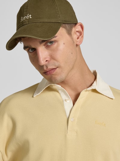 Männermodel trägt Basecap mit Label-Stitching von Forét im Denim-Look in Olivgrün, Sticklogo, Nahaufnahme Oberkörper, verstellbarer Riegel.
