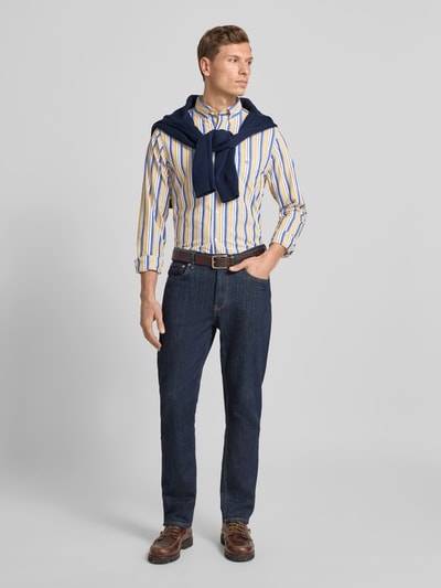 Männermodel draagt Vrijetijdsoverhemd met knoopsluiting van Gant in puur katoen, regular fit, button-downkraag, borstzak, labelstitching, ruglengte maat M 77 cm, schouderbreedte 44 cm, mouwlengte 67 cm, verticale strepen in geel, blauw en wit, Ganzkörperansicht von vorne.