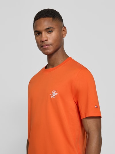 Männermodel trägt Regular Fit T-Shirt aus reiner Baumwolle von Tommy Hilfiger in Orange mit Logo-Stitching, Nahaufnahme Oberkörper.