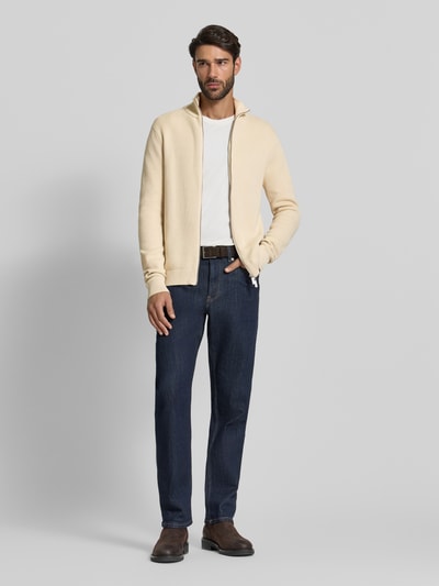 Männermodel trägt Regular Fit Strickjacke aus reiner Baumwolle Modell 'DANE' von SELECTED HOMME in Beige, unifarben, Stehkragen, Ganzkörperansicht von vorne.