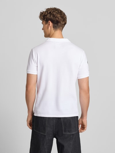 Männermodel trägt Regular Fit Poloshirt mit Label-Patches von Superdry aus Reine Baumwolle, weiße Farbe, Rückenlänge 68 cm, Ganzkörperansicht Rückansicht.