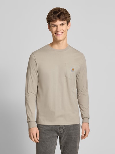 Männermodel trägt Longsleeve mit Brusttasche und Label-Detail von Carhartt Work In Progress, Baumwolle, Regular Fit, Frontansicht Oberkörper.