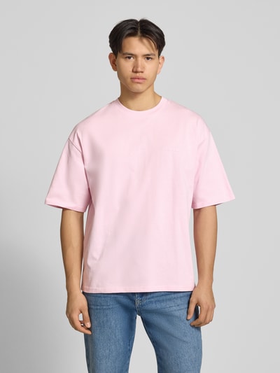 Männermodel trägt Oversized T-shirt mit logo en ronde hals van REVIEW in lichtroze, puur katoen, heren, oversized fit, ruglengte maat M 68 cm, Ganzkörperansicht von vorne.