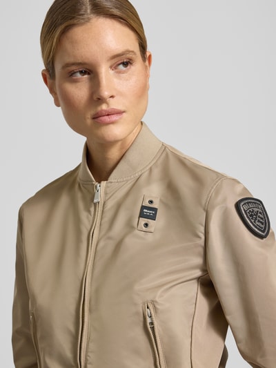 Frauenmodel trägt Bomberjacke mit Stehkragen Modell 'LAURIE' von Blauer Usa in Beige, Reißverschlusstaschen, Label-Patches, Nahaufnahme Oberkörper. Rückenlänge 57 cm, Schulterbreite 44 cm, Brustweite 43 cm, Ärmellänge 62 cm, Loose-Fit.