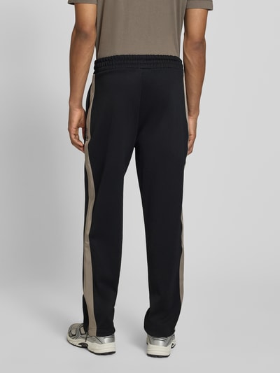 Männermodel trägt Regular Fit Jogpants mit Baumwoll-Anteil Modell 'DOLOS' von HUGO, schwarz mit Kontraststreifen, Ganzkörperansicht Rückansicht.