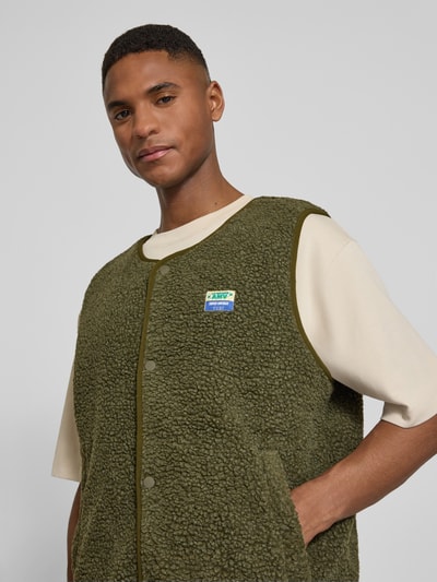 Männermodel trägt Straight Fit Weste mit Logo-Patch Modell 'Hoktown' von American Vintage, Kunstfell in Oliv, Nahaufnahme Oberkörper.