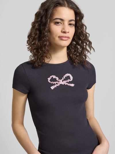 Frauenmodel trägt T-Shirt mit Rundhalsausschnitt Modell 'PREPPY HEART' von Review, schwarz, fein gerippt, rosa Herzmotiv, Nahaufnahme Oberkörper. Damen T-Shirt aus Baumwoll-Mix mit Stretch-Anteil, gerader Schnitt, Rückenlänge bei Größe S 49 cm.