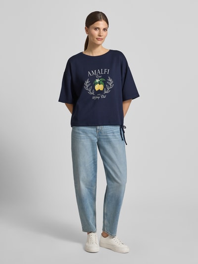 Frauenmodel trägt Relaxed Fit T-Shirt mit Logo-Print von Christian Berg Woman, Elastischer-Material-Mix mit Modal-Anteil, Rundhalsausschnitt, Dunkelblau, lockere Passform, jeans kombiniert, Ganzkörperansicht von vorne.
